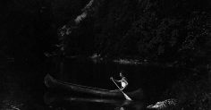 A man embarks on a canoe journey across a serene lake, marking a personal rite of passage.