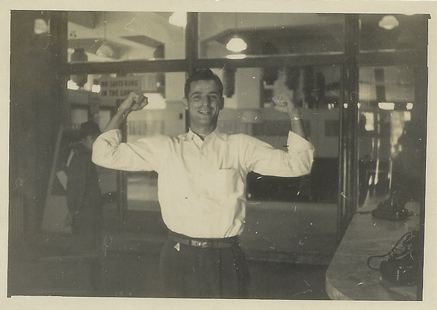 A confident man is flexing his arms in front of a window.