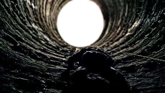 In a dark tunnel, a man shines his flashlight while climbing.