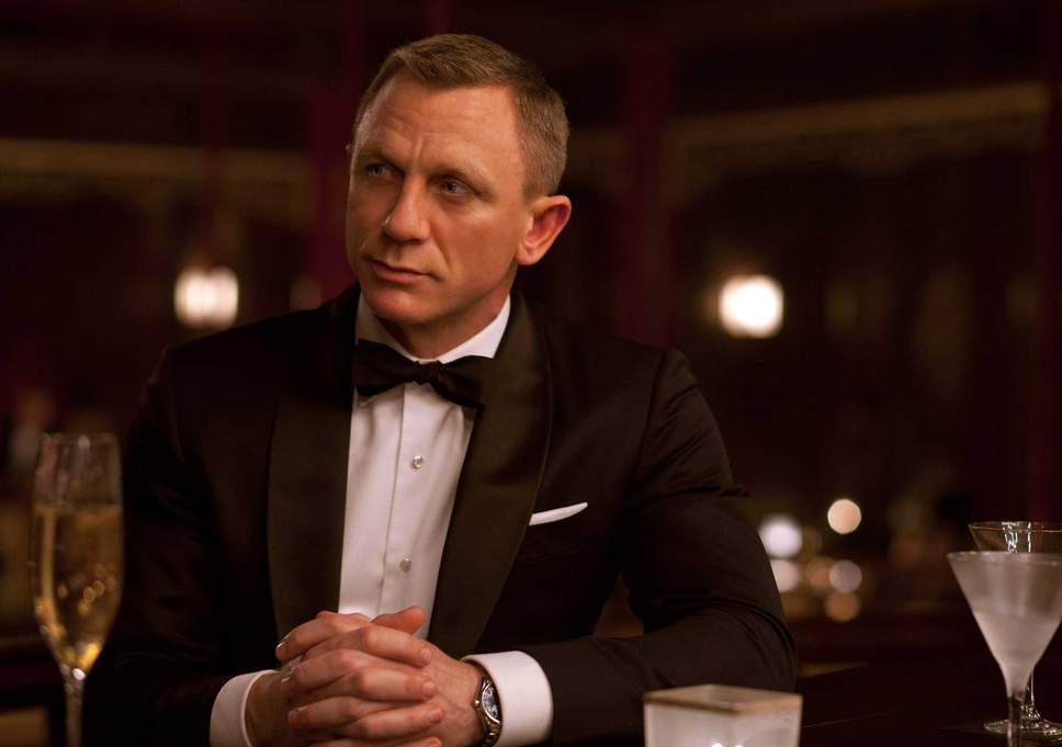 James Bond, with his suave savoir-faire, sits at a table in his iconic tuxedo.