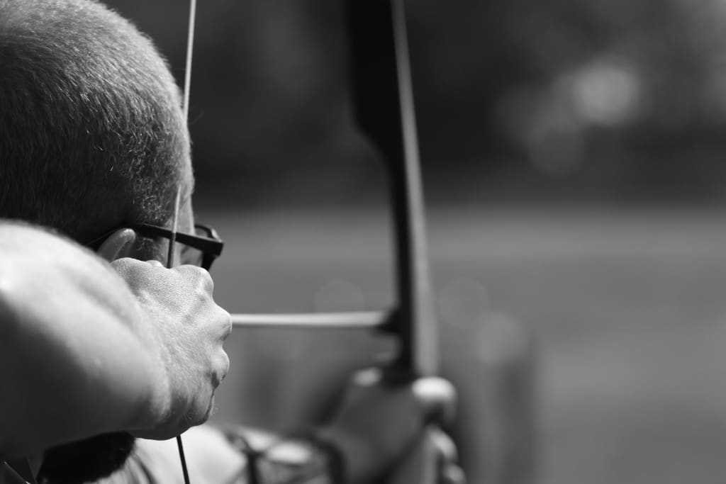 The man with glasses is focused on aiming at the archery target, embodying the essence of precision.