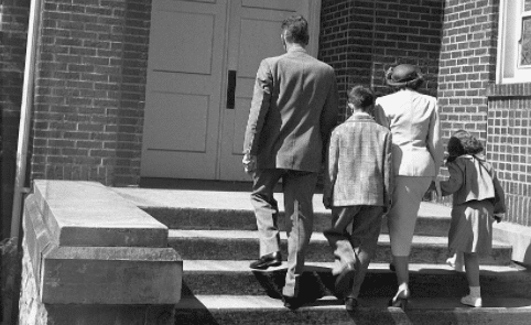 Black and white photo of a family walking down the steps of a church, showcasing their beliefs.