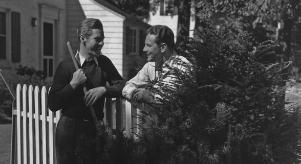 Two neighbors standing next to a white picket fence.