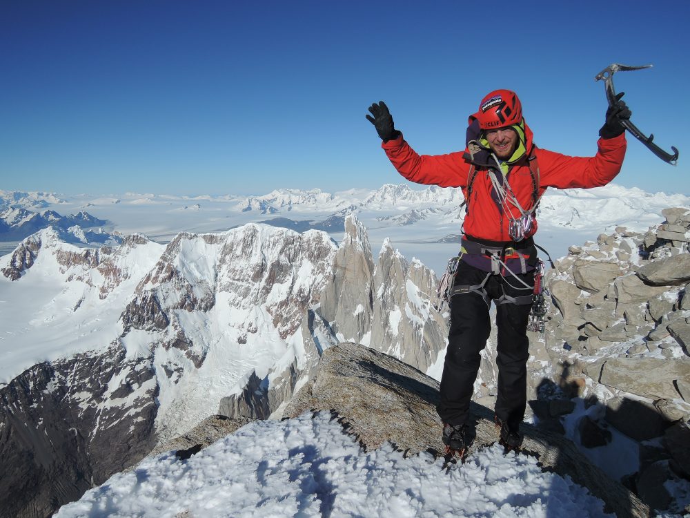 A climber standing on top of a mountain with his arms raised in celebration.