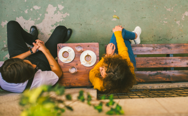 A man and woman sitting on a wooden bench, people enjoying each other's company.