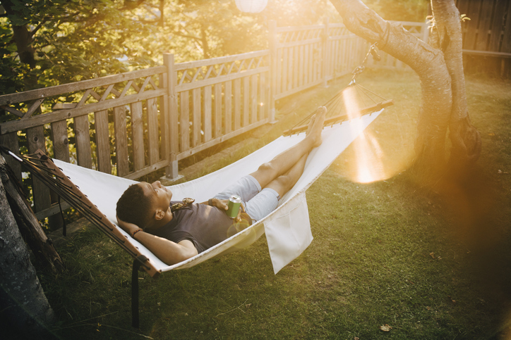 A man lounging in a hammock, listening to a podcast.