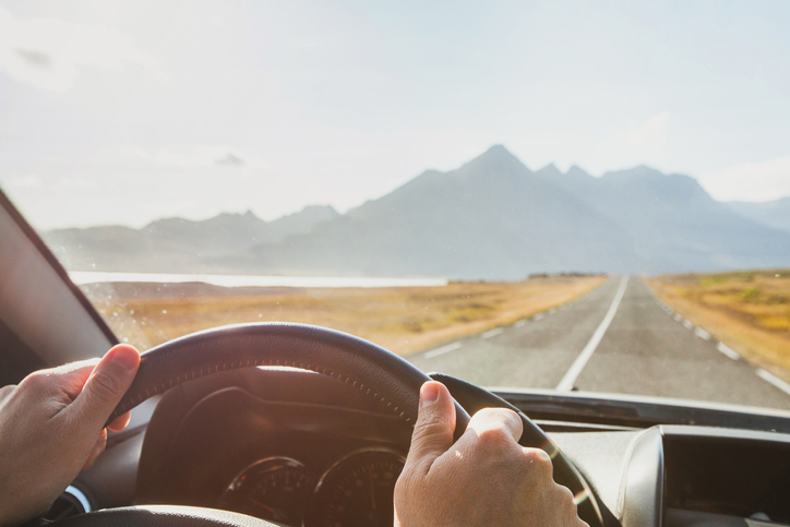 A person driving a car with mountains in the background.