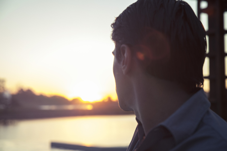 A man is looking out over a body of water, contemplating life's regrets.
